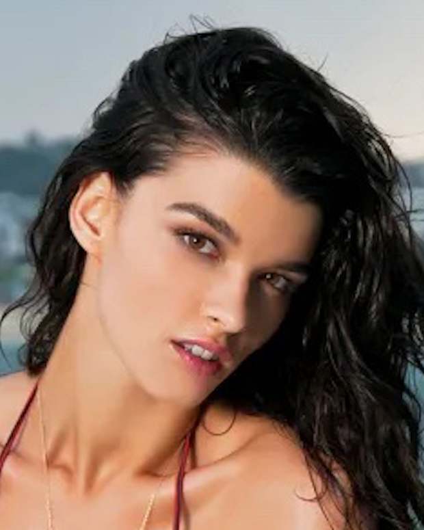 Crystal Renn poses in a red bikini and wet hair before the skyline of a beachside town in Australia.
